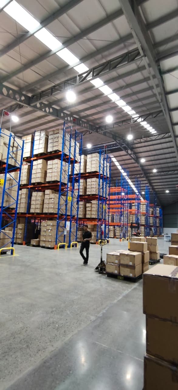 Rak heavy duty TAP di gudang logistik dan distribusi — aktivitas pemindahan pallet dengan hand pallet
